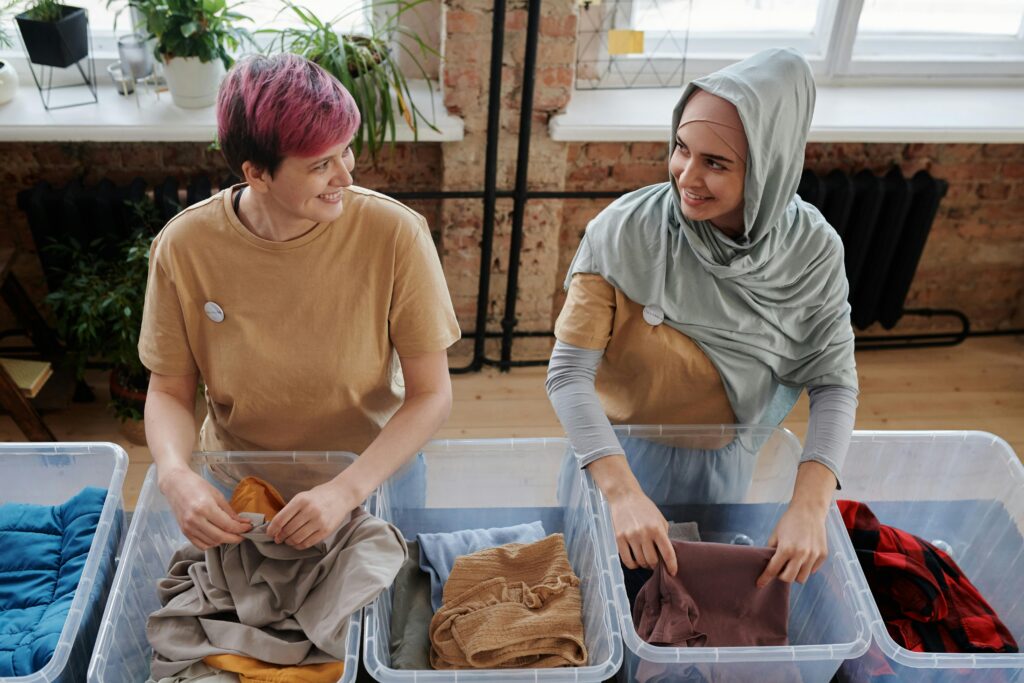 Two smiling volunteers sorting clothes into boxes for charity at an indoor location.