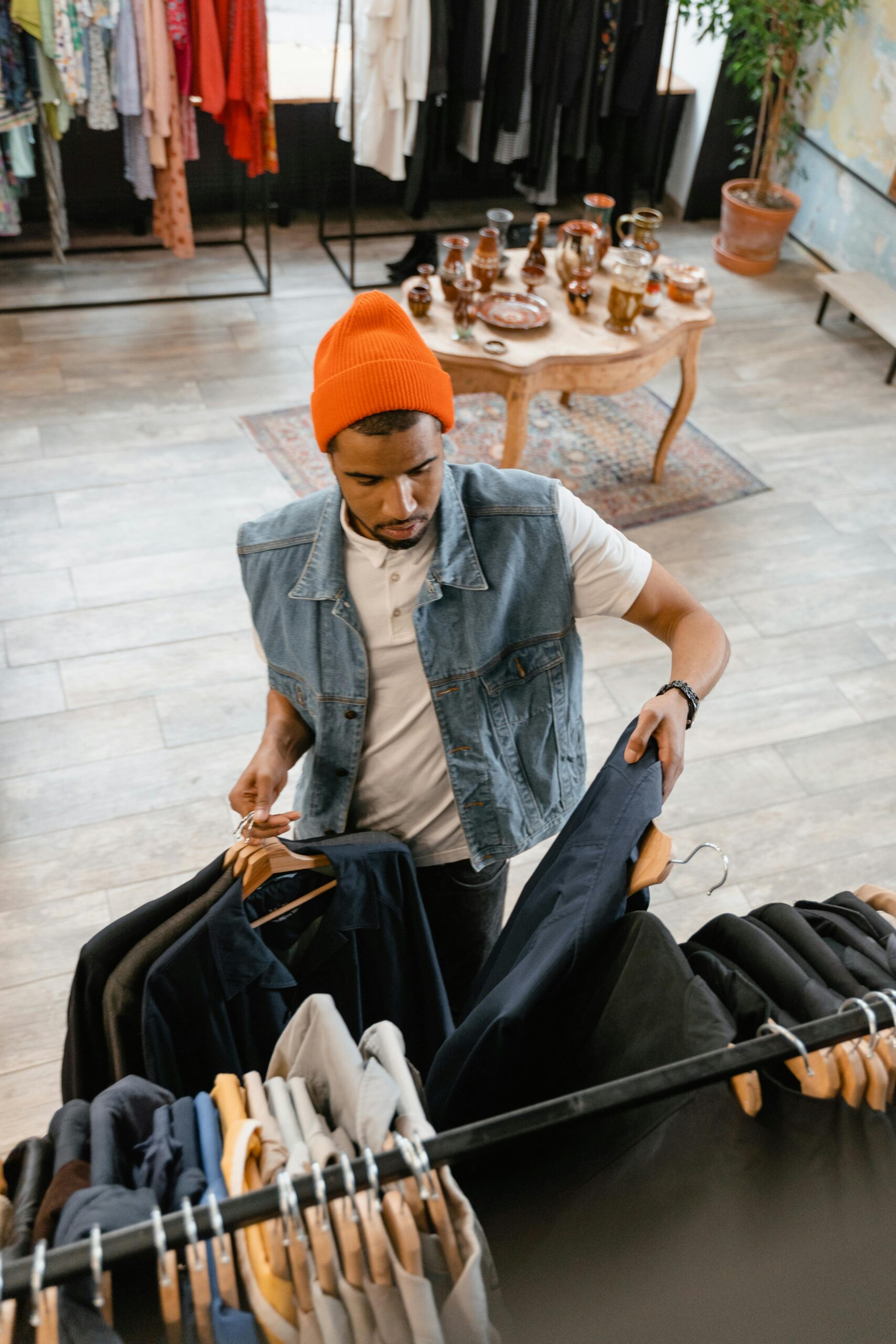 Stylish man in denim vest and beanie shopping for clothes in trendy store.